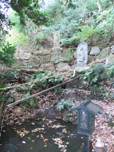 緑に囲まれた小さい池の上に不動の石像が立つ