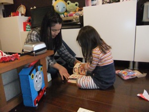 真由喜がプレゼントに囲まれ、ゆり子と一緒に絵本を読む