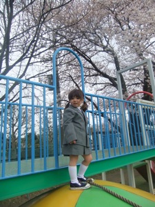 真由喜が桜の前に大型遊具に立つ