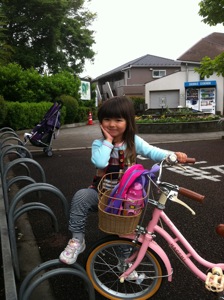 真由喜が自転車を持って、足を自転車置き場に載せて、手で顔を支える