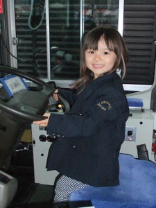 バス運転手の真由喜 真由喜が子供サイズの制服のジャケットを来て、川崎市バスの運転席に座る
