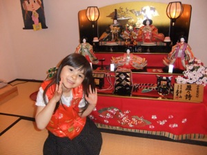 ちゃんちゃんこを着ている真由喜が雛人形の前にポーズしている