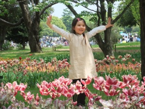 真由喜が花畑で手を挙げて立つ