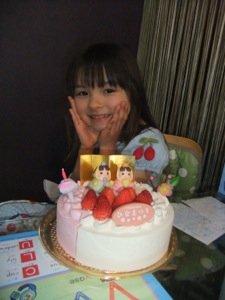 笑顔の真由喜がケーキの後ろに座っている。