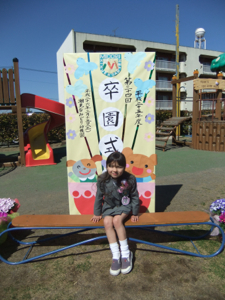 真由喜が卒園式と書いてある看板の前に座っている。