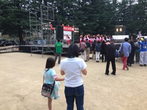公園で、ゆり子と真由喜が舞台の上の踊りを観賞する